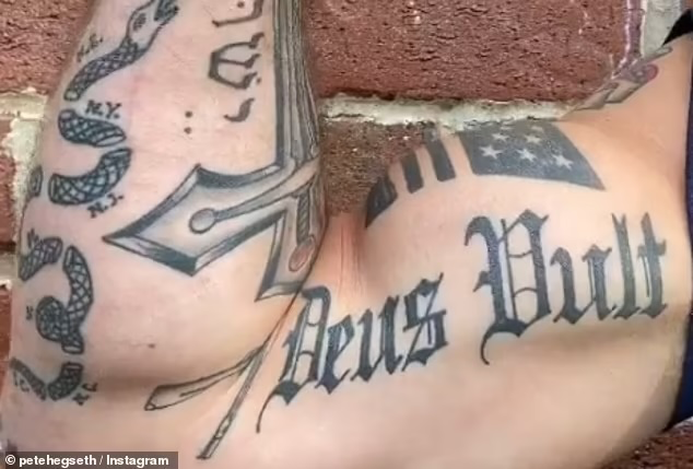 close-up of a forearm tattoo reading 'Deus Vult' in gothic script